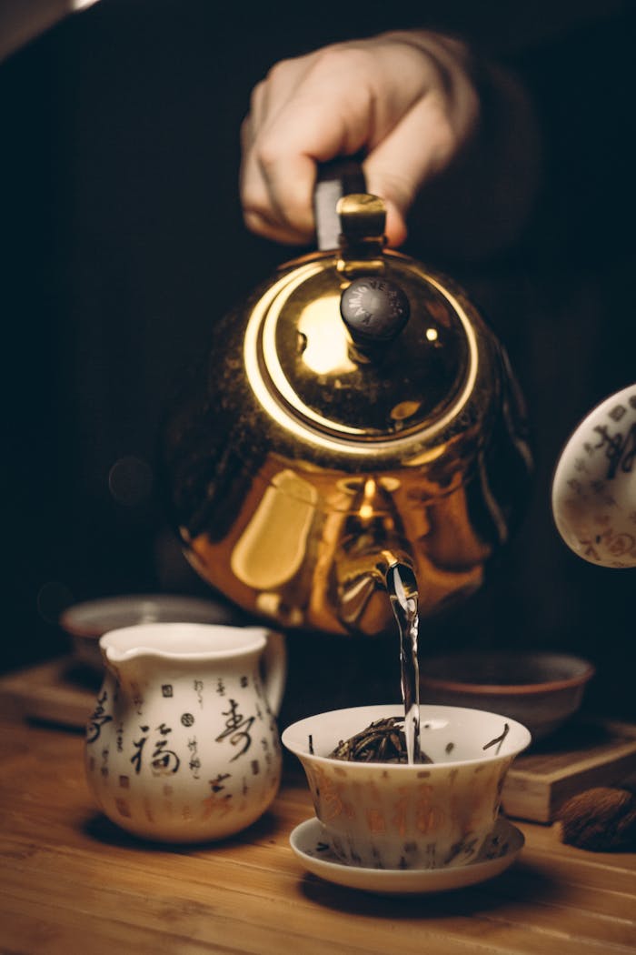 Close-up of a golden teapot pouring tea into a cup with Chinese calligraphy.